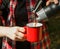 Tourist hands pour coffee from a thermos into a metal red cup