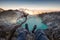 Tourist hanging legs on crater Kawah Ijen with emerald lake at s