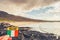 Tourist holding badge with Irish flag and sign Ireland in focus. Rough stone in the ocean, stunning sandy beach and hill in the