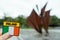 Tourist holding badge with National flag and sign Ireland in focus, Galway Hooker monument in Eire square out of focus