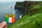 Tourist holding badge with sign Ireland and Irish flag in focus, Cliff of Moher out of focus.