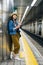 Tourist holding cellphone standing on the platform in the subway station waiting for train. young lady traveler using phone