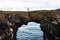 Tourist jumps over a natural rock bridge in Arnarstapi, Iceland