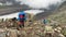 A tourist with a large backpack climbs up a mountain path past a scattering of stones and boulders