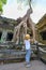 Tourist looking at Ta Prohm famous jungle tree roots embracing Angkor temples, revenge of nature against human buildings, travel