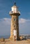 A tourist looks at a phone while sitting on stone steps at the foot of the historic sandstone Whitby West Pier Lighthouse