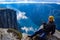 Tourist man on the edge above Lysefjorden. Wonderful mountain landscape with clouds reflected in blue water. Norway