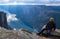 Tourist man on the edge above Lysefjorden. Wonderful mountain landscape with clouds reflected in blue water. Norway