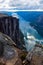 Tourist man on the edge above Lysefjorden. Wonderful mountain landscape with clouds reflected in blue water. Norway