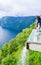 Tourist man looks at the water falling from the platform. Eagles Road viewpoint. Landscape of Geirangerfjord and Seven Sisters