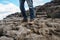 Tourist in old worn out hiking boots and blue jeans in a rough mountain terrain. Long journey concept. Legs in old shoes on hard