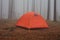 Tourist orange tent in the fog in the forest