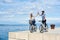 Tourist pair, man and woman with bicycles on high paved stone sidewalk near sea water on sunny day