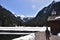 A tourist passing by a small water dam with wooden house near by tourist path heading directly towards to Murg lakes