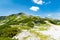 Tourist path in Slovenia mountains near Vogel. Path of top of mountain, green grass, tress, blue sky. Hiking in Europe. Triglav na