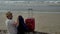 Tourist with a red suitcase came to the sea, sitting on the sand of the beach takes off his jacket