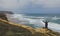 A tourist on a rocky shore looks in the distance at the raging ocean and surfers. Atlantic Ocean. Portugal.