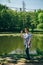 Tourist senior beautiful woman in blue jeans and striped T-shirt standing on the bank of the lake surrounded by park