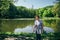 Tourist senior beautiful woman in blue jeans and striped T-shirt standing on the bank of the mountain lake surrounded by forest,