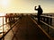 Tourist sit on mole handrail and takes pictures.Wooden boardwalk