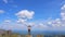 A tourist stands against the background of a blue sky with clouds and raises his hands up to the sky.