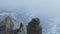 A tourist stands on the ledge of a sheer cliff against the background of a valley partially covered with snow. Hiking.