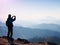 Tourist takes photos with smart phone on peak of rock. Dreamy fogy landscape, spring orange pink misty sunrise in a beautiful