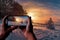 Tourist taking photo of sunset over winter landscape with covered in snow pine and fir trees against dramatic evening light. Snowy