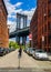 Tourist taking pictures of iconic Manhattan Bridge and Empire State Building view from Washington Street in Brooklyn, New York