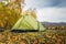 Tourist tent on the grass in a picturesque secluded place on the river bank among rocky mountains on warm autumn day, close-up.