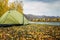 Tourist tent on the grass in a picturesque secluded place on the river bank among rocky mountains on warm autumn day, close-up.