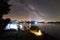 Tourist tent, two camping chairs and campfire on lake shore at night