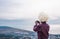 Tourist in traditional caucasian hat made of white sheepskin takes a picture of the sea landscape and the city of Gagra, Abkhazia