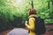 Tourist traveler with backpack into road at summer green forest, view back girl hiker in yellow hoody looking and enjoying