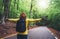 Tourist traveler with backpack standing with raised hands, girl hiker view from back looking into road at forest