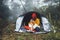 Tourist traveler in camp tent hugging red shiba inu on background froggy rain forest, hiker woman kiss puppy dog in mist nature