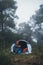 Tourist traveler ralaxing in camp tent in froggy mist forest, lonely hiker woman enjoy nature trip, green trekking tourism