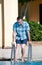 Tourist and traveler is standing next to swimming pool of hotel resort, holds on to handrail, watching and checking to water.