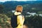 Tourist traveler with yellow backpack standing on green top on mountain, hiker view from back looking on hills and mountain river