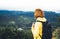 Tourist traveler with yellow backpack standing on green top on mountain, hiker view from back looking on hills and mountain river