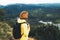 Tourist traveler with yellow backpack standing on green top on mountain, hiker view from back looking on hills and mountain river