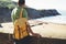 Tourist traveler with yellow backpack standing on green top on mountain, hiker view from back looking on ocean, man enjoying natur