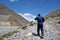 Tourist with trekking sticks climbs uphill, passing along the Kali Gandaki River.