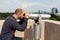 Tourist using panoramic binoculars telescope looking at metropolitan urban city