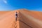 Tourist walking on the scenic dunes of Sossusvlei, Namib desert, Namib Naukluft National Park, Namibia. Afternoon light. Adventure