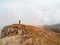 Tourist walks on mountain near abyss edge on high altitude under cloudy sky in foggy day. Man on high rock near precipice edge