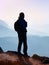 Tourist in windcheater with sporty backpack and poles in hands stand on rocky view point and watching into deep misty valley