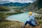 A tourist woman with a backpack sits on top of the mountain and looks at the confluence of the rivers Chui and Katun