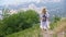 Tourist woman with backpack walking down on mountain path on city panorama view. Traveling woman descending on mountain