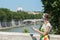 Tourist woman in flower sundress holding tablet and looking at Rome Tiber bridge and masterpiece dome